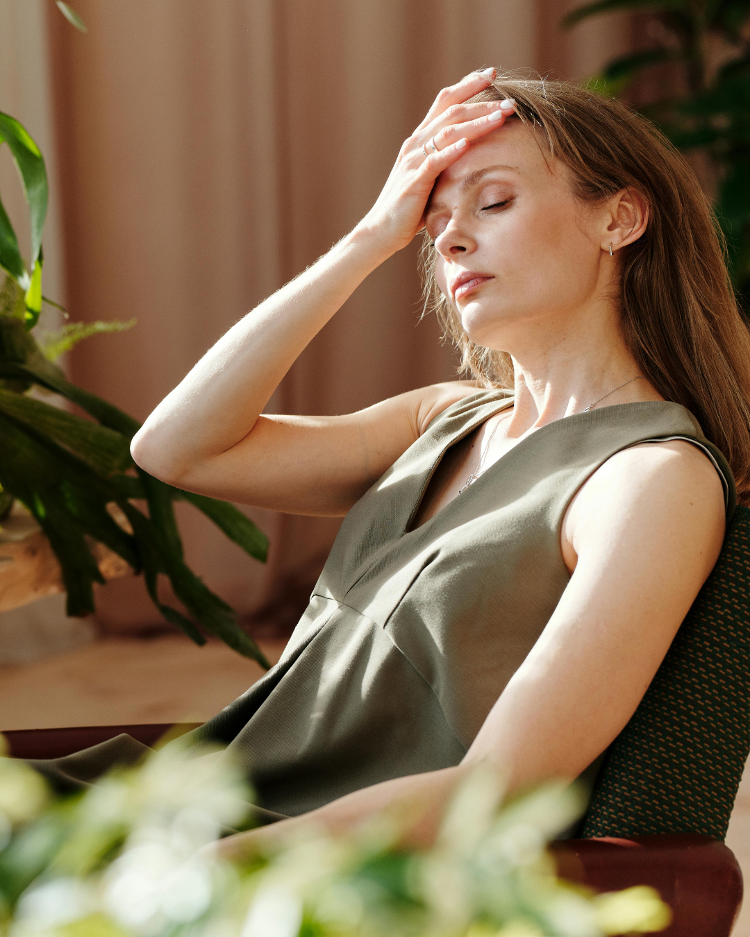 women leaning back on a chair and holding her head with one hand and closed eyes