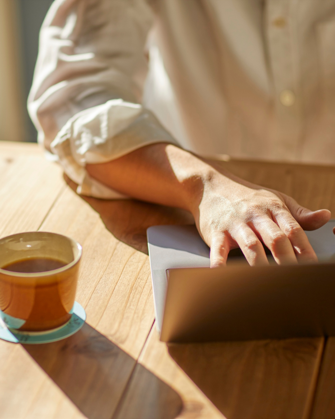 Focussed typing hand on a laptop with a mug of coffee on the side